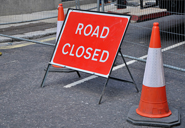 picture of a tarmac road with orange cones and a red road closed sign